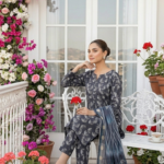 Model sitting on a white bench in a terrace setting wearing the ginkgo maze 3 piece premium lawn suit, showcasing the charcoal indigo matching printed shirt and trousers with a draped patterned dupatta.