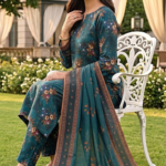 Model sitting on a white garden chair wearing a teal spruce 3 piece elegent summer lawn suit, displaying the matching teal blue printed shirt, trousers, and a gracefully draped patterned dupatta on the grass.