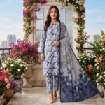 Woman wearing a pastel ice blue floral printed 3 piece lawn suit with matching patterned trousers and a blue leaf design dupatta.
