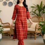Model walking indoors wearing a matching 2-piece crimson red traditional premium lawn co-ord set with yellow accents.