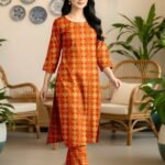 Model walking indoors wearing a matching 2-piece sunset orange traditional premium lawn co-ord set with geometric tile patterns.