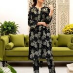 Model posing near a green sofa in the black variant of the monarch foil 2 piece premium summer lawn suit with olive prints.