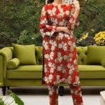 Model posing near a green sofa in the red variant of the monarch foil 2 piece premium summer lawn suit with beige prints.