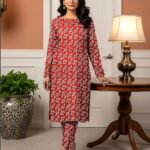 Model standing by a table lamp wearing the crimson red variant of the ivy bunch 2 piece premium summer lawn suit with off-white foliage prints.