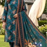 Model posing in a grassy garden lawn wearing a matching 3-piece deep teal spruce elegent summer lawn suit with tan prints and a geometric bordered dupatta.
